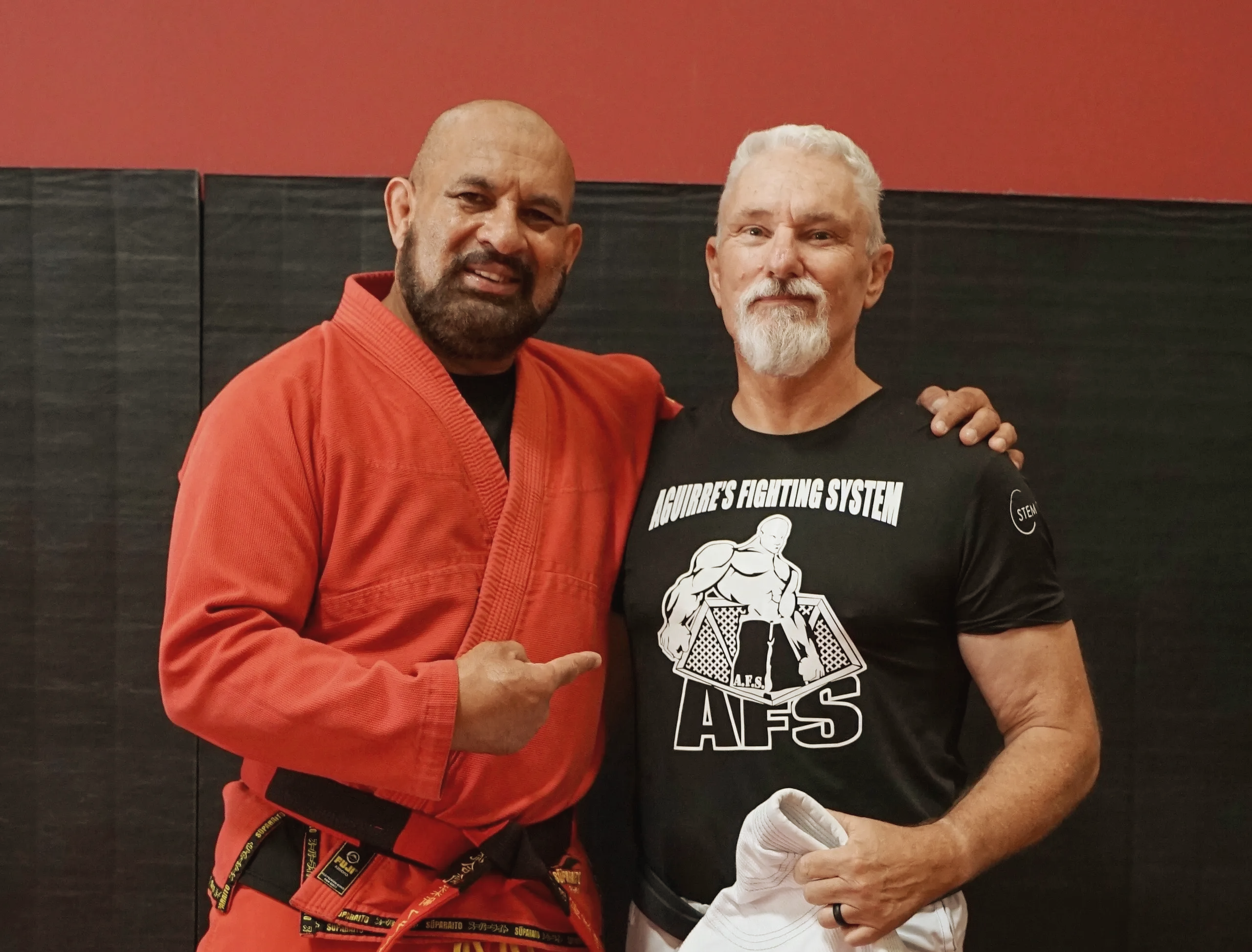 Two men posing in martial arts attire, one in a red gi and the other in a black t-shirt.
